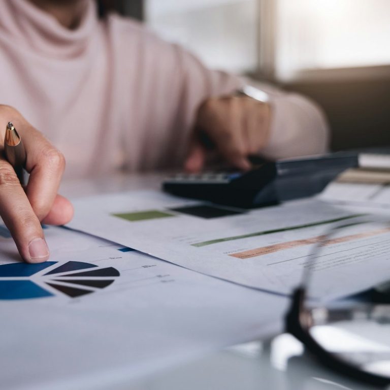 Person analysing charts and graphs with a calculator and documents on a desk.